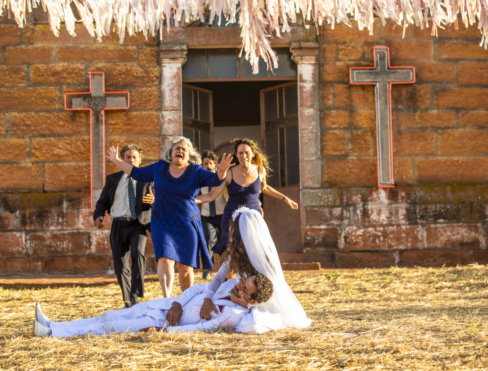 Maria Da Paz (Juliane Paes) e Amadeu (Marcos Palmeira) no chão. Miroel (Luiz Carlos Vasconcellos), Nilda (Jussara Freire), Vicente (Álamo Facó) e Ticiana (Áurea Maranhão) correm na direção deles em A Dona do Pedaço