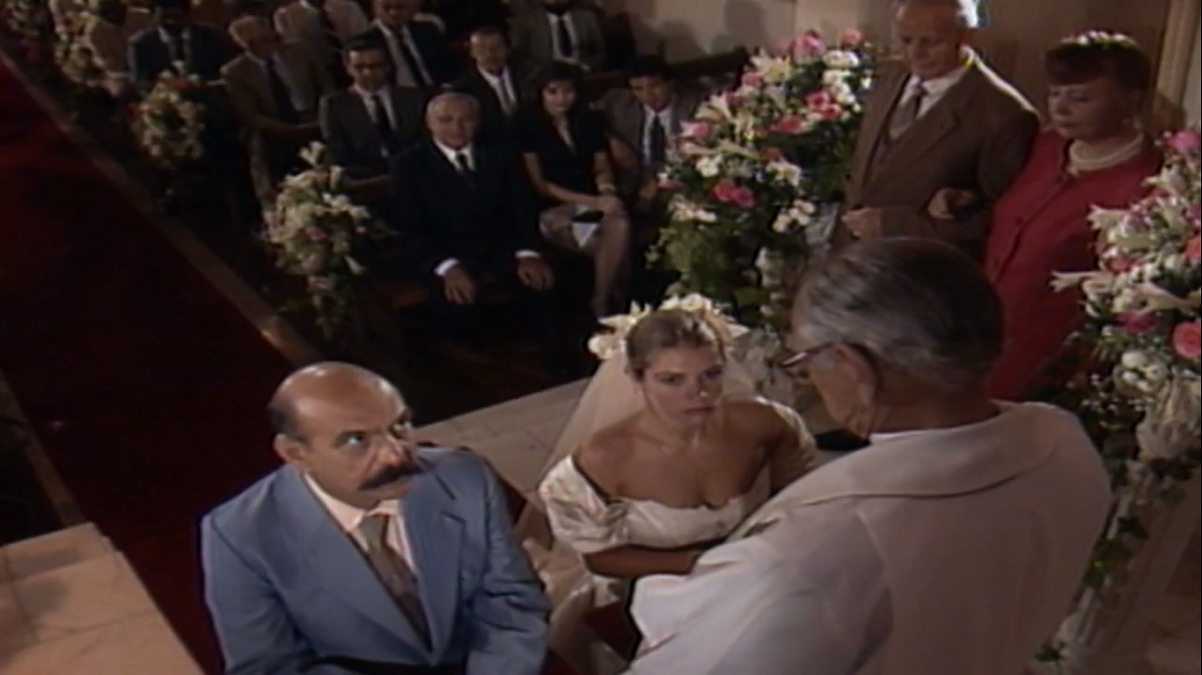 Sassá (Lima Duarte) e Marlene (Tássia Camargo) diante do Padre Elísio (Brandão Filho) na cerimônia de seu casamento em O Salvador da Pátria