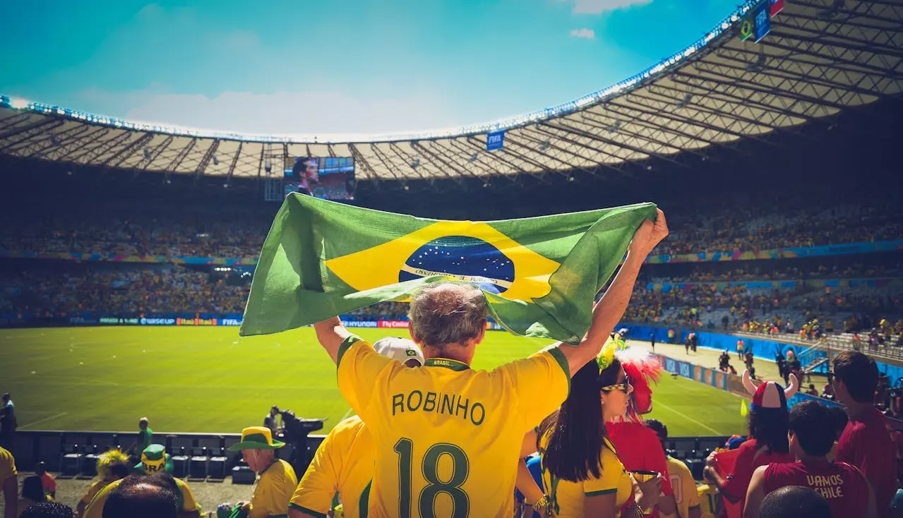 Homem hasteando bandeira do Brasil dentro de estádio de futebol