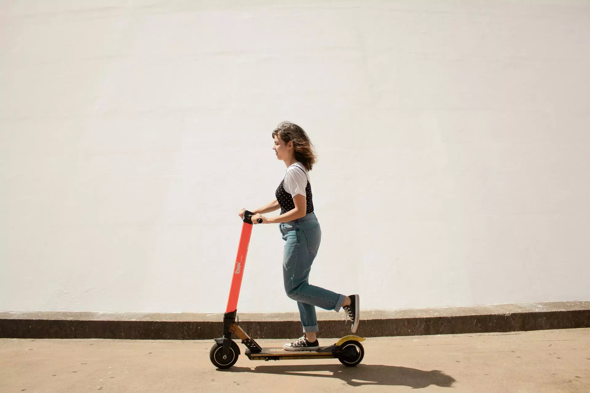 Mulher de camisa branca e jeans em scooter vermelho e preto de tênis